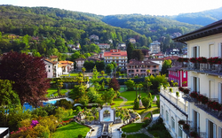 Blick auf eine gepflegte Gartenanlage mit Gebäuden und bewaldeten Hügeln im Hintergrund.