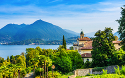 Landschaft mit Palmen, Villa und Blick auf einen See und Berge im Hintergrund.