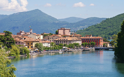 Stadtansicht mit Fluss, historischen Gebäuden und Bergen im Hintergrund.