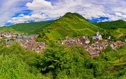Panorama einer grünen Hügellandschaft mit Dorf und Fluss im Hintergrund.