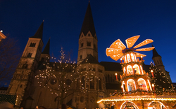 Weihnachtsmarkt mit beleuchteter Weihnachtspyramide vor einer Kirche bei Nacht im Hintergrund.