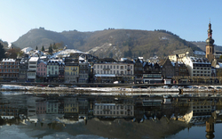 Stadtansicht mit Fluss und schneebedeckten Hügeln im Hintergrund.