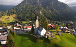 Luftaufnahme eines Dorfes mit Kirche und Bergen im Hintergrund.
