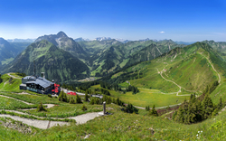 Panorama der Alpen mit grünen Hügeln und einem Berghaus.