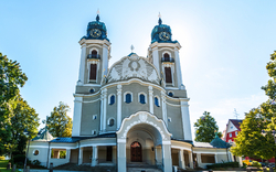Barockkirche mit zwei hohen Türmen und blauer Kuppel, umgeben von Bäumen.