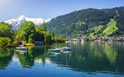 Bergsee mit Segelbooten, umgeben von Bergen und Wald, unter klarem Himmel.