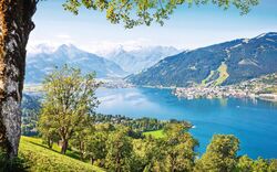 See mit Gebirge im Hintergrund und grüne Landschaft im Vordergrund.