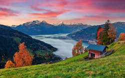 Hütte auf grüner Wiese vor Alpenlandschaft bei Sonnenuntergang.