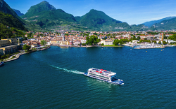 Ein Schiff fährt über einen See mit Bergen im Hintergrund.
