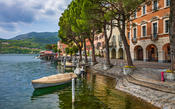 Hafenpromenade mit Booten, Bäumen und farbigen Gebäuden am See.