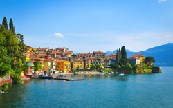 Italienisches Dorf am See mit bunten Häusern und Bergen im Hintergrund.