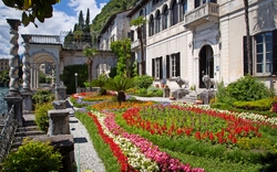 Garten mit bunten Blumen vor einem historischen Gebäude an einem sonnigen Tag.