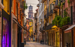 Enge Gasse in italienischer Stadt mit historischen Gebäuden und einem Turm im Hintergrund.