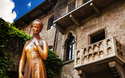 Statue einer Frau vor einem historischen Gebäude mit Balkon und Efeu.