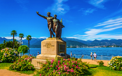 Statue vor einem See mit Bergen im Hintergrund bei klarem Himmel.