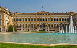 Große, historische Villa mit Brunnen im Vordergrund.