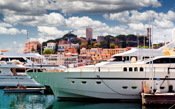Yachten im Hafen vor einer Stadt mit alten Gebäuden und Türmen unter bewölktem Himmel.