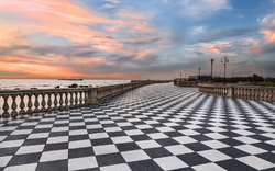 Promenade mit Schachbrettmusterboden bei Sonnenuntergang am Meer in Livorno, Italien.
